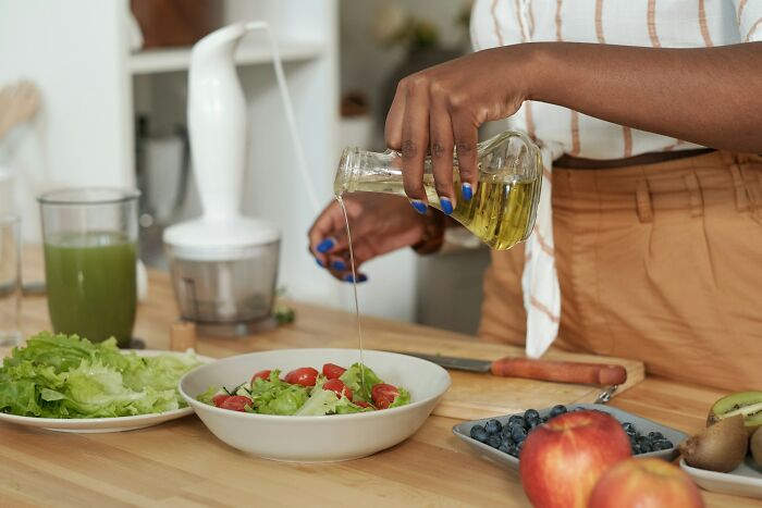 Person pouring olive oil on fresh salad in kitchen, illustrating work secrets about baristas doctors and plumbers.