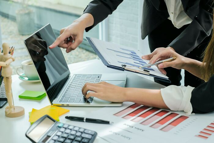 Two professionals analyzing business charts and data on a laptop and clipboard, revealing work secrets insights.