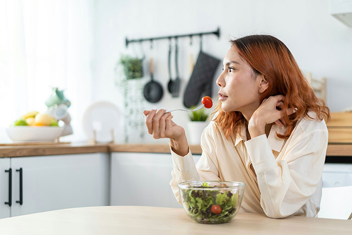 Woman eating salad in kitchen, reflecting on domestic chores and no longer playing mommy in household duties. Woman eating salad in kitchen, reflecting on domestic chores and no longer playing mommy in household duties.