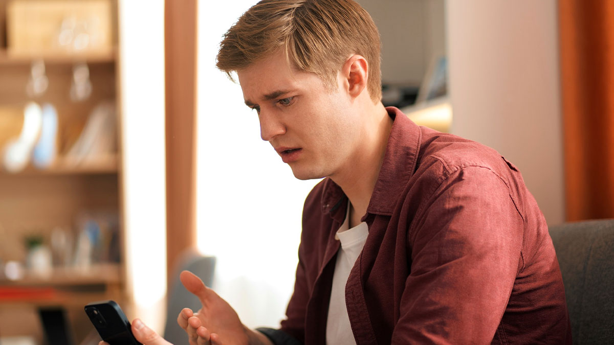 Young guy looking irked while holding phone, learning that his friend likes him after she cries and sits on his lap