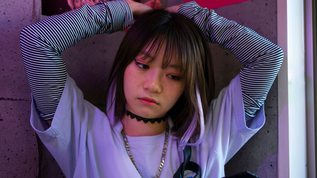 Young woman looking upset under purple lighting, reflecting emotions related to fangirling over a K-Pop band.