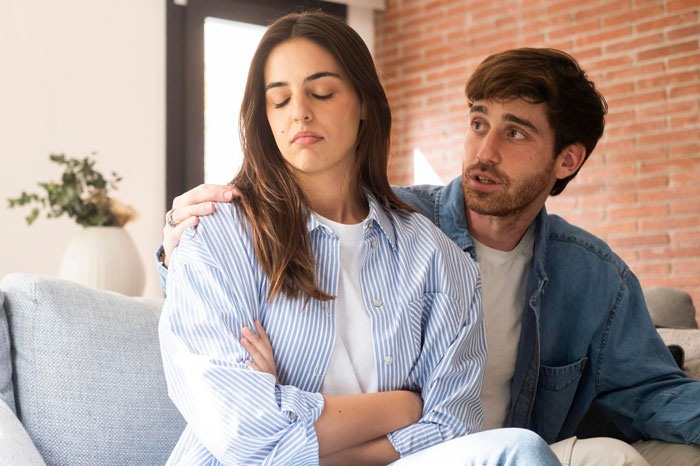 Young man mocking girlfriend for fangirling over a K-pop band while she looks upset and avoids eye contact at home.
