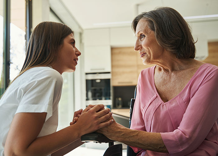 Mother and daughter holding hands and talking intensely in a modern kitchen, capturing a tense relationship moment.