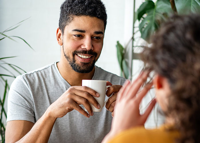 Man smiling and holding a cup while on a date, capturing a moment in a daughter’s relationship affected by a mom’s actions.