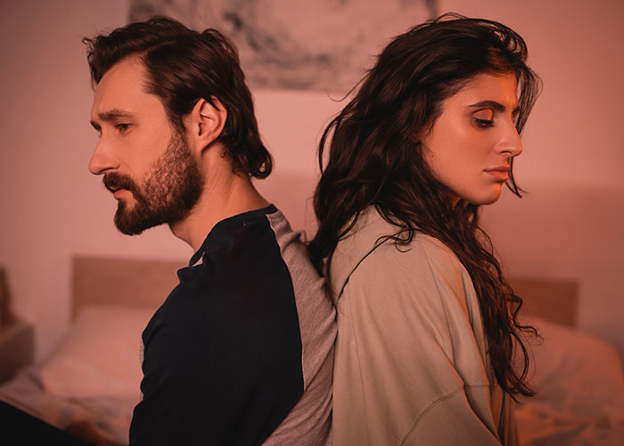 Couple sitting back to back in a dimly lit room, showing tension after a mom destroys daughter’s happy relationship.