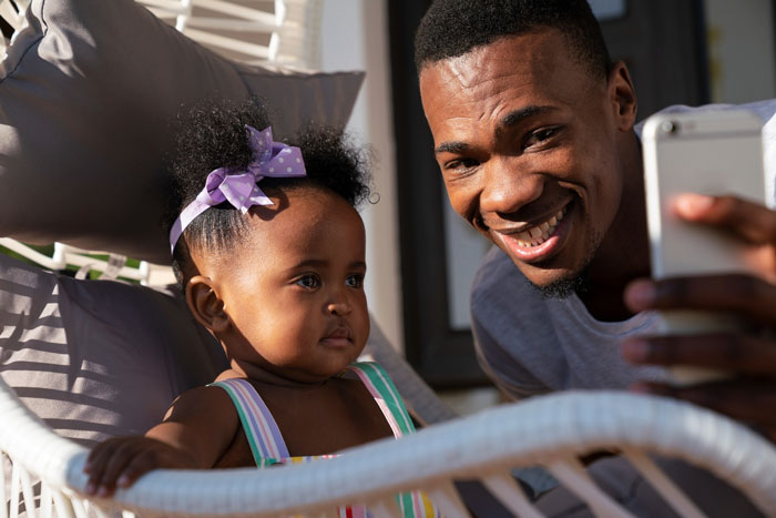 Father taking a selfie with baby girl wearing purple bow, highlighting baby’s name honoring culture and heritage conflict.