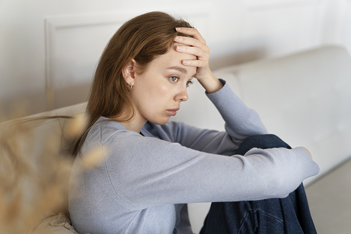 Young woman sitting on couch looking stressed and upset after parents demand she give up amazing career opportunity to golden-child sister Young woman sitting on couch looking stressed and upset after parents demand she give up amazing career opportunity to golden-child sister