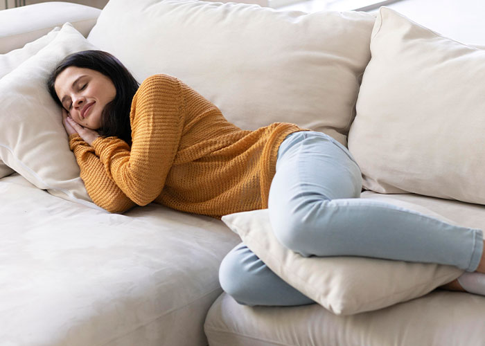Woman in a cozy sweater resting on a couch, illustrating unusual wellness habits experts recommend for better health.