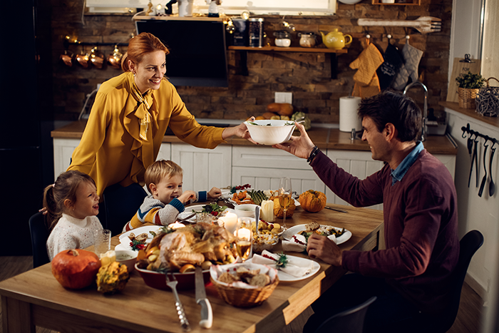 Family sharing Thanksgiving food at a cozy kitchen table with a roasted turkey and autumn decorations.