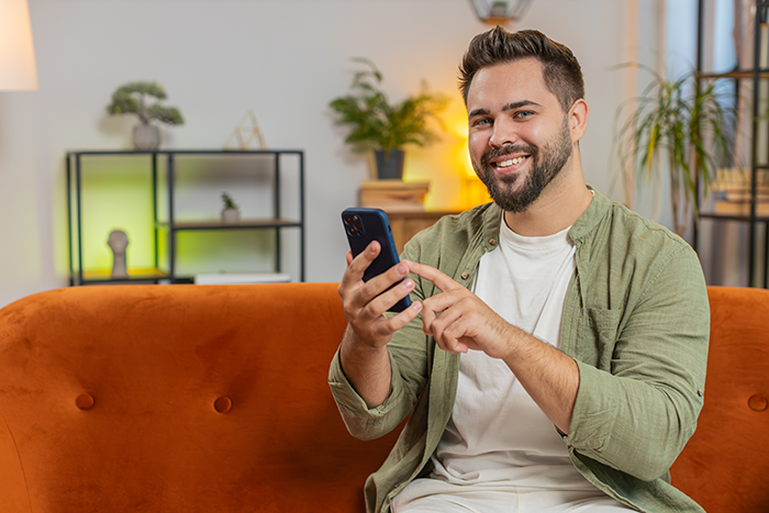 Man happy holding phone on orange couch, smiling confidently after ex-wife caught cheating in modern living room. Man happy holding phone on orange couch, smiling confidently after ex-wife caught cheating in modern living room.