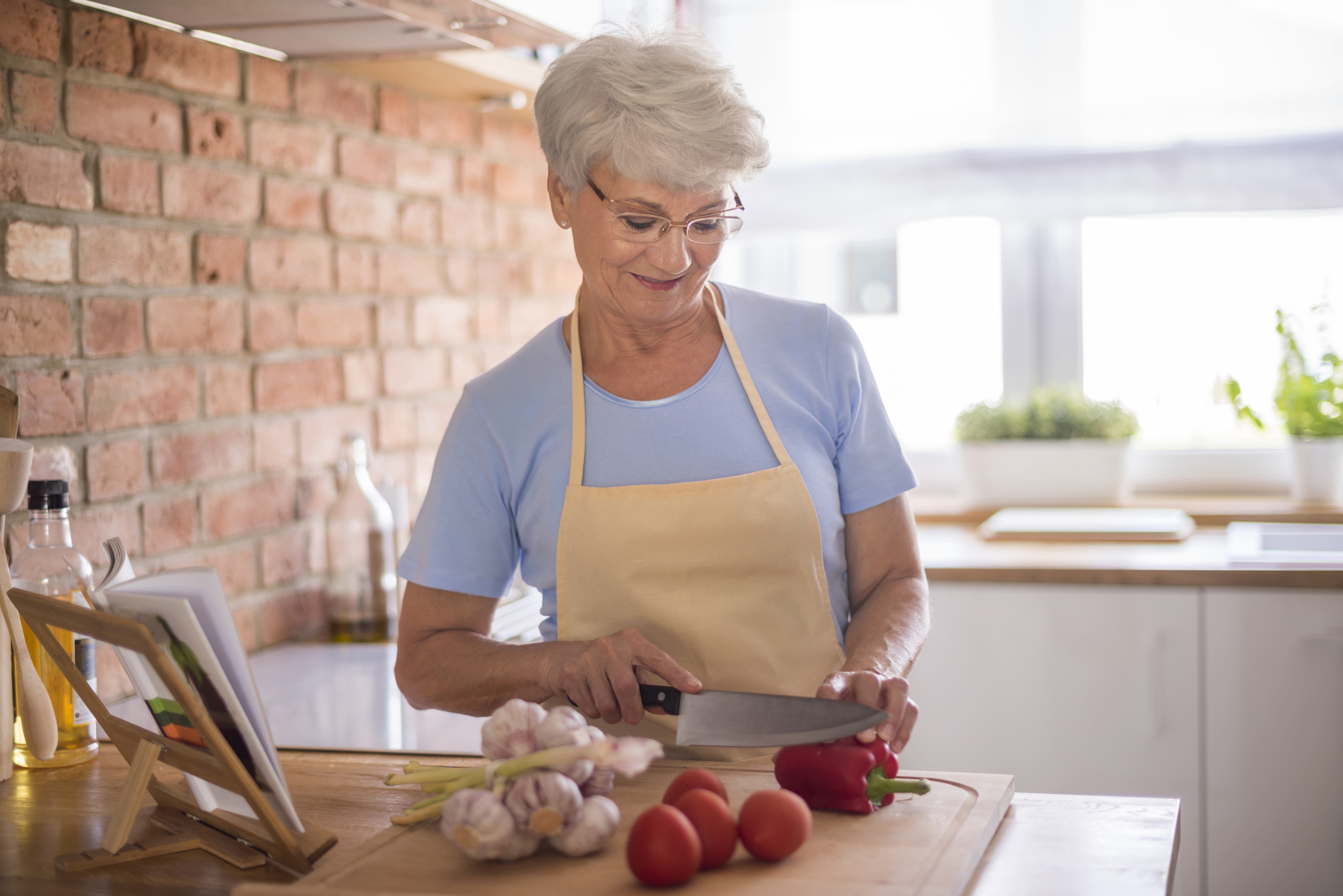 Older woman preparing vegetables in a kitchen, illustrating MIL’s cooking concerns impacting pregnant woman’s Thanksgiving plans. Older woman preparing vegetables in a kitchen, illustrating MIL’s cooking concerns impacting pregnant woman’s Thanksgiving plans.