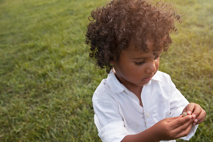 Young child with curly hair wearing a white shirt standing on grass, symbolizing family health fund and plastic surgery conflict.