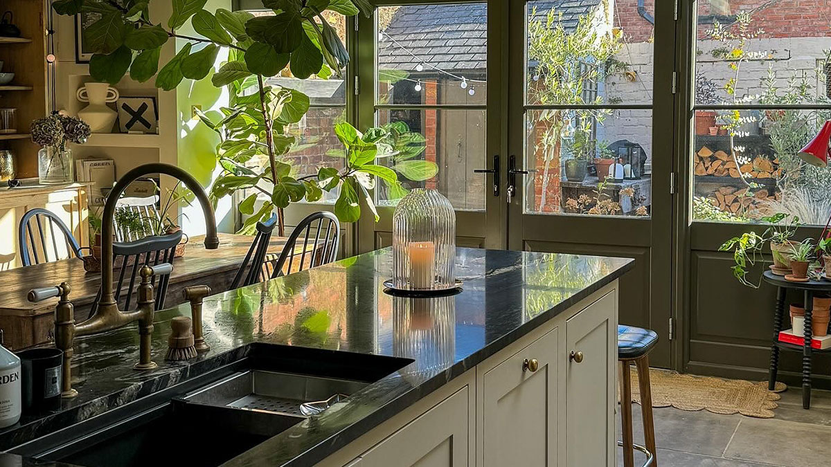 Modern kitchen renovation with green accents, natural light, plants, and a sleek marble island countertop and seating area.