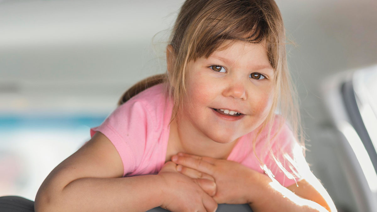 Young girl smiling indoors with hands clasped, representing a daughter and nanny with Spanish lessons theme.