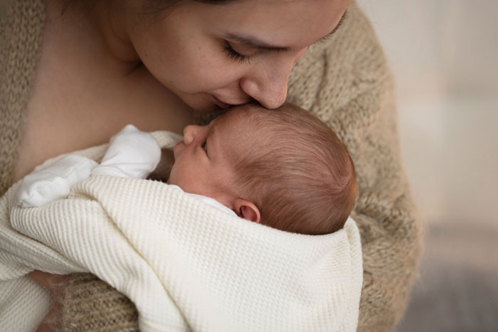 Indian grandmother holding newborn baby wrapped in white blanket, looking closely at the child in a cozy setting. Indian grandmother holding newborn baby wrapped in white blanket, looking closely at the child in a cozy setting.