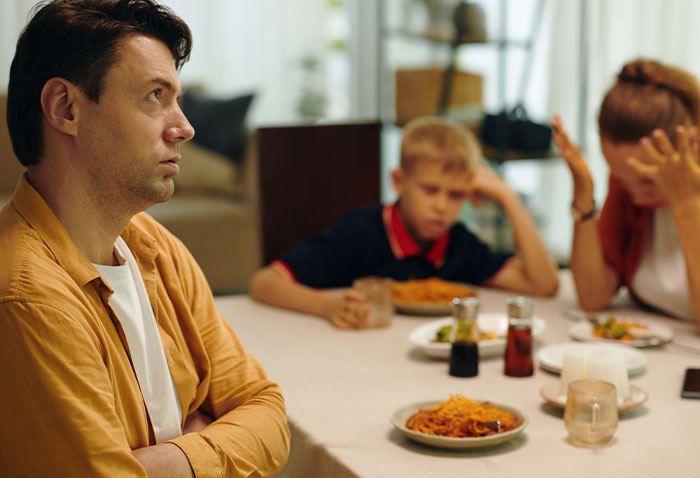 Man looking frustrated at Thanksgiving table while wife and son show signs of distress during family dinner tension