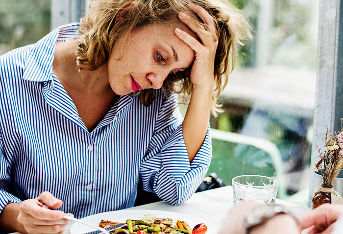 Stressed woman sitting at table with food, reflecting tension after family Thanksgiving celebration with a major tantrum incident.