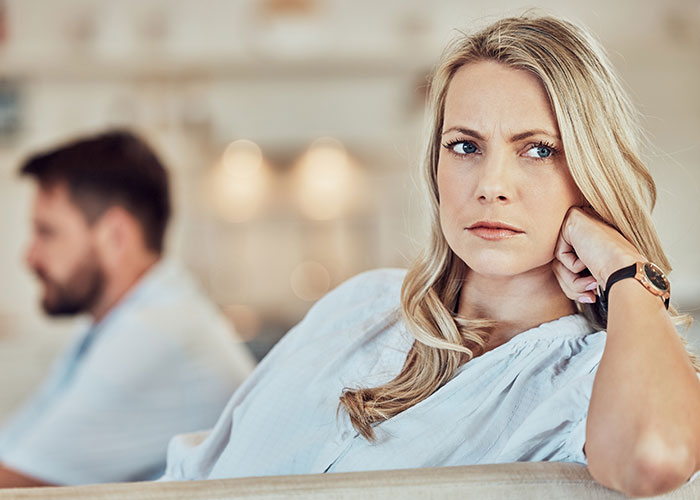 Wife looking suspicious and upset while man sits in the background, highlighting master’s degree lie discovery story.