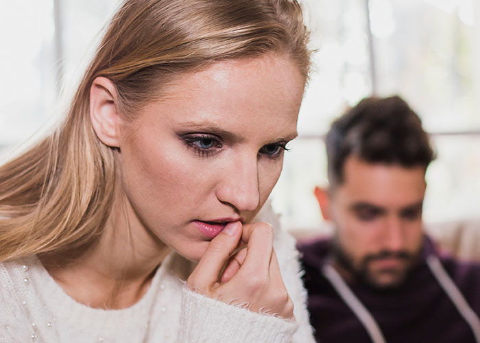 Worried woman thinking deeply while man sits in background, illustrating a master’s degree lie and truth discovery.