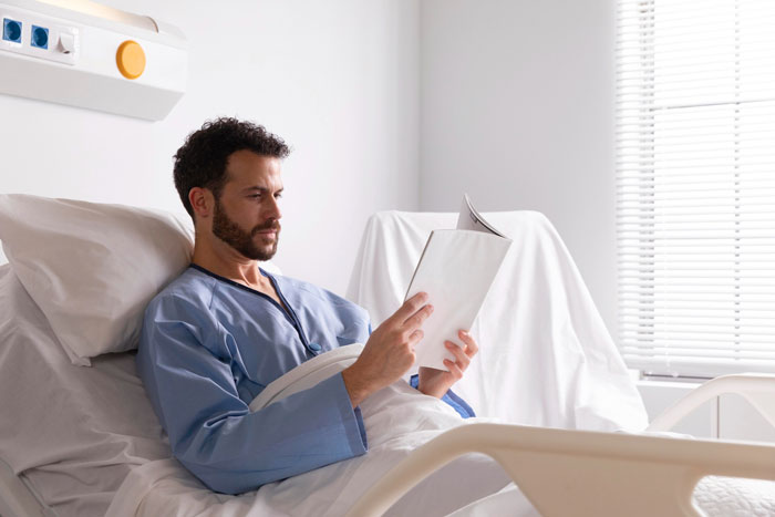 Man in hospital bed wearing gown, reading medical documents, related to life-threatening condition concerns. Man in hospital bed wearing gown, reading medical documents, related to life-threatening condition concerns.