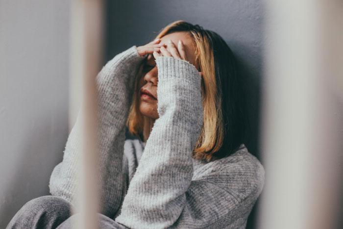 Woman in gray sweater sitting against wall covering face, representing obsession and life-threatening condition concerns. Woman in gray sweater sitting against wall covering face, representing obsession and life-threatening condition concerns.