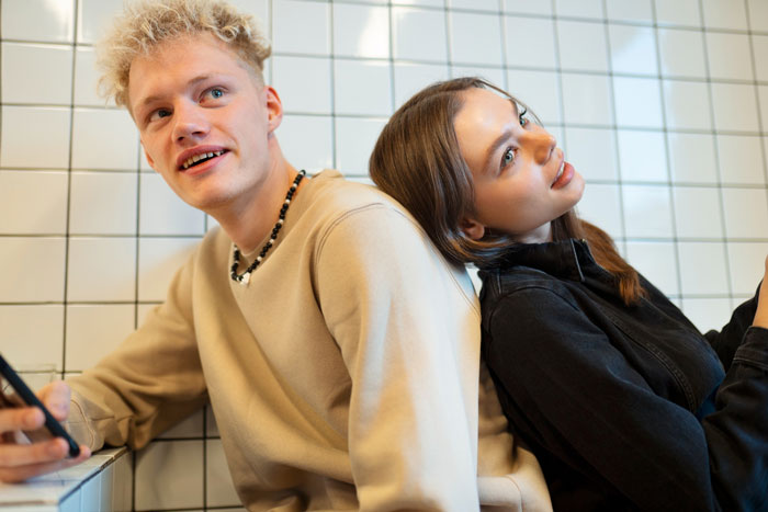 Young man and woman sitting back to back indoors, reflecting on husband retirement and children finances planning. Young man and woman sitting back to back indoors, reflecting on husband retirement and children finances planning.