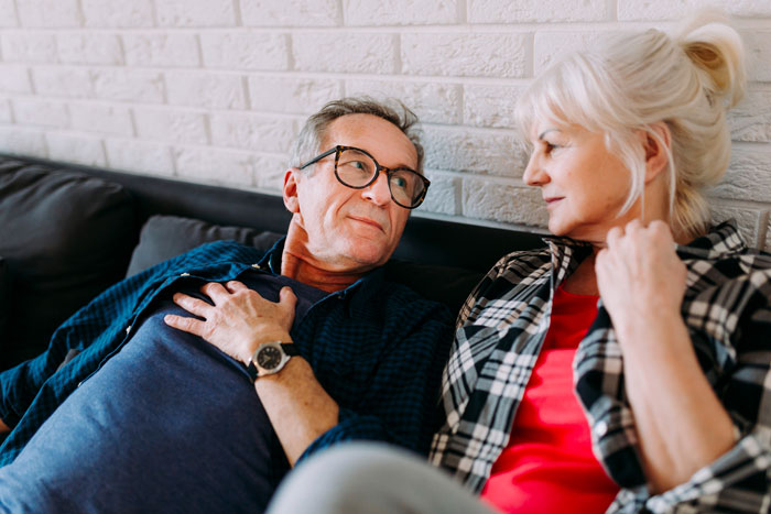 Older couple discussing husband retirement and children finances while sitting on a couch in a cozy living room setting Older couple discussing husband retirement and children finances while sitting on a couch in a cozy living room setting