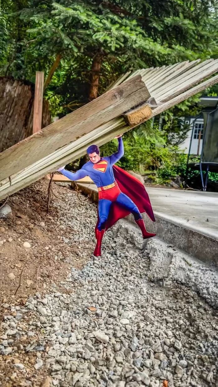 Paper cutout of Superman by Rudy Willingham lifting wooden beam outdoors on gravel near greenery. Paper cutout of Superman by Rudy Willingham lifting wooden beam outdoors on gravel near greenery.