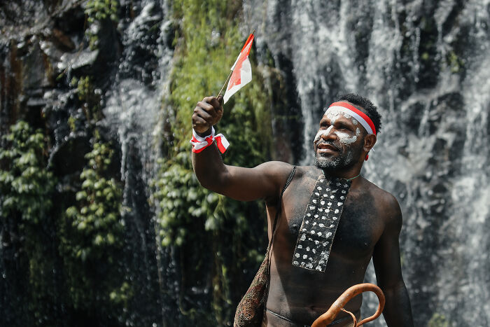 Man in traditional attire with face paint holding a flag near a waterfall, symbolizing internet rabbit holes taking over lives.