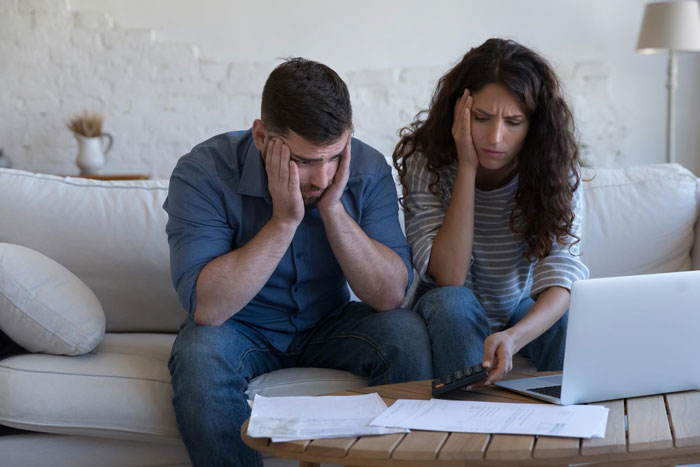Entitled siblings looking stressed and upset while reviewing papers and using a calculator on a living room couch. Entitled siblings looking stressed and upset while reviewing papers and using a calculator on a living room couch.