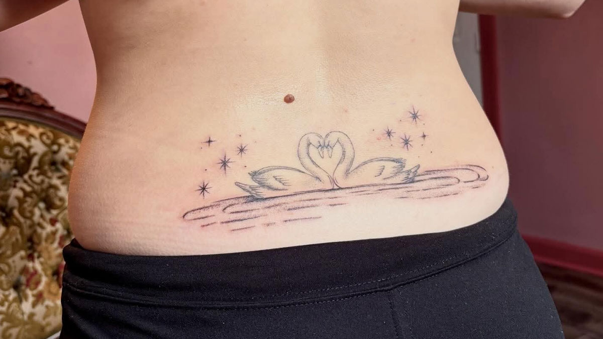 Lower back tattoo of two swans forming a heart shape surrounded by stars, an example of hilariously unfortunate tattoos.