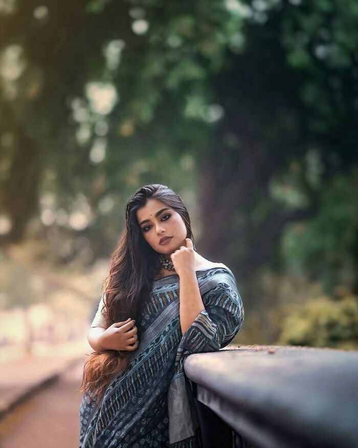Young woman in traditional attire posing outdoors with a serene background, reflecting positive stereotypes of various countries.