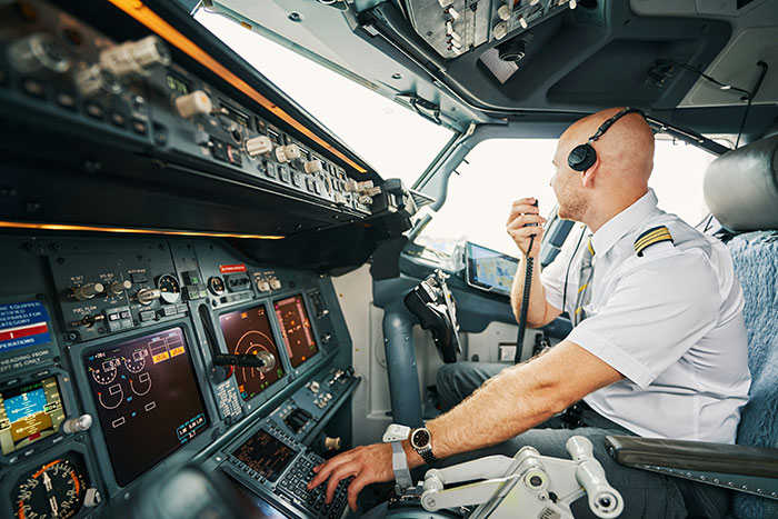 Pilot in airplane cockpit using radio controls, illustrating secrets about planes and flying from a passenger's view.