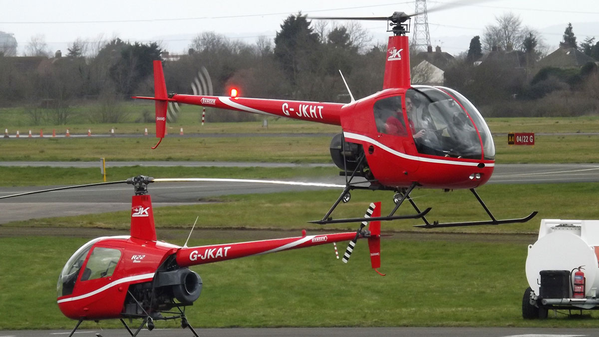 Two red helicopters on a grassy airfield showcasing unique aspects of planes and flying for passengers.