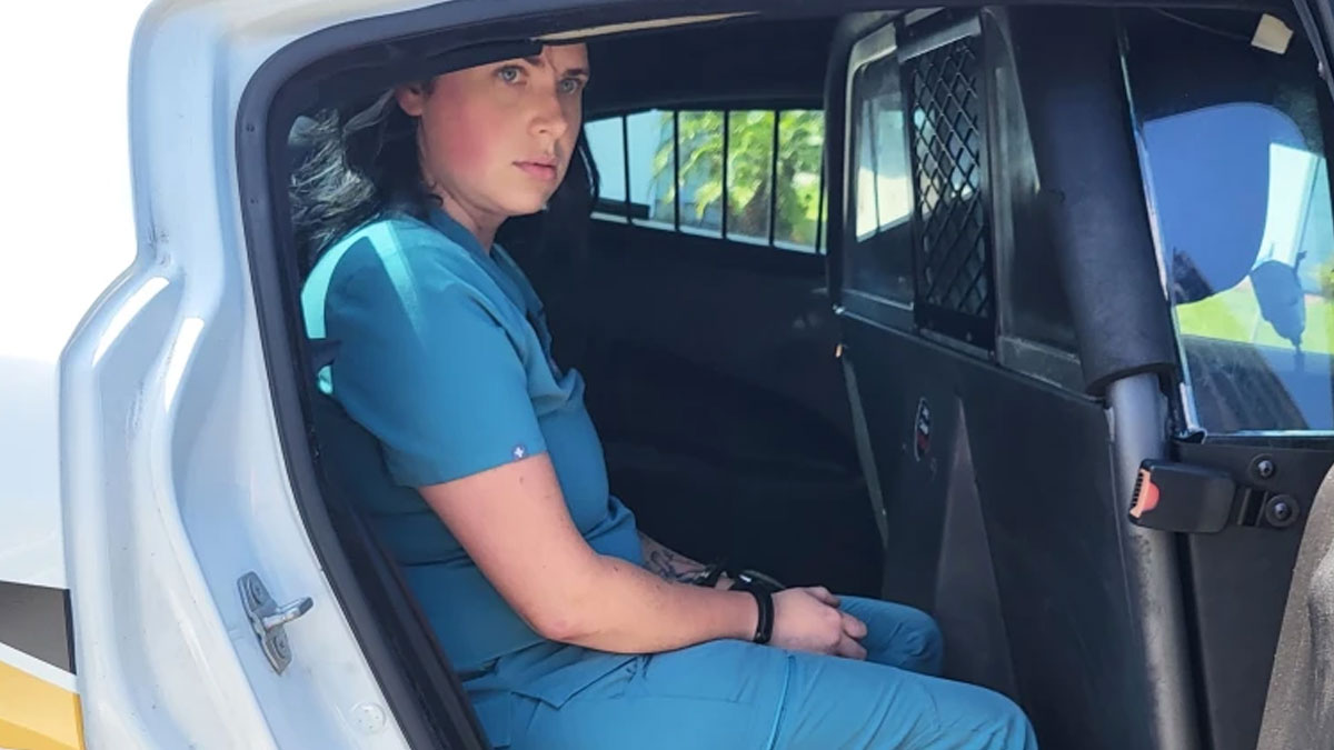 Woman wearing blue scrubs sitting in the back of a police vehicle, illustrating this IG page sharing daily facts and interesting stories.