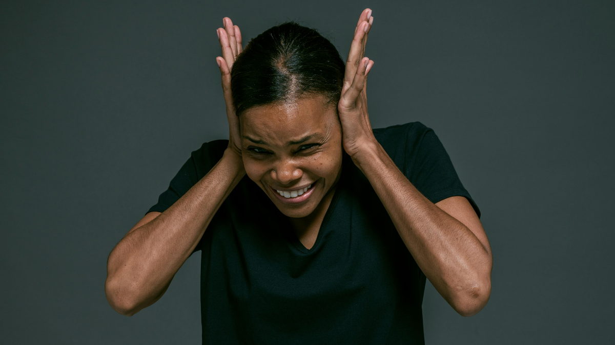 Woman in black shirt appearing distressed, holding her head, illustrating the concept of mind working against you.