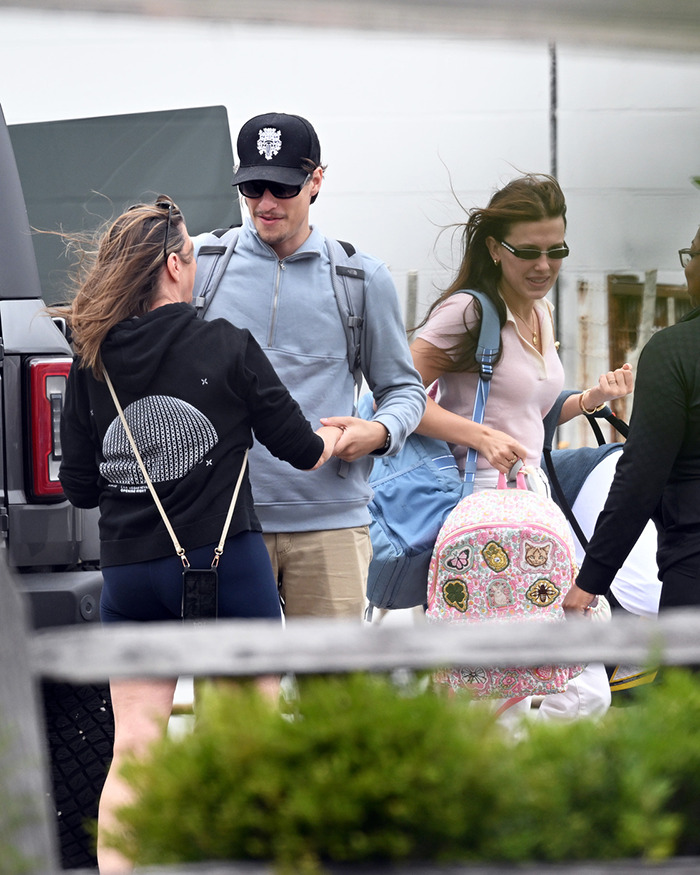 Jake Bongiovi and Millie Bobby Brown walking outdoors, Millie carrying a colorful baby bag with patches and designs. Jake Bongiovi and Millie Bobby Brown walking outdoors, Millie carrying a colorful baby bag with patches and designs.