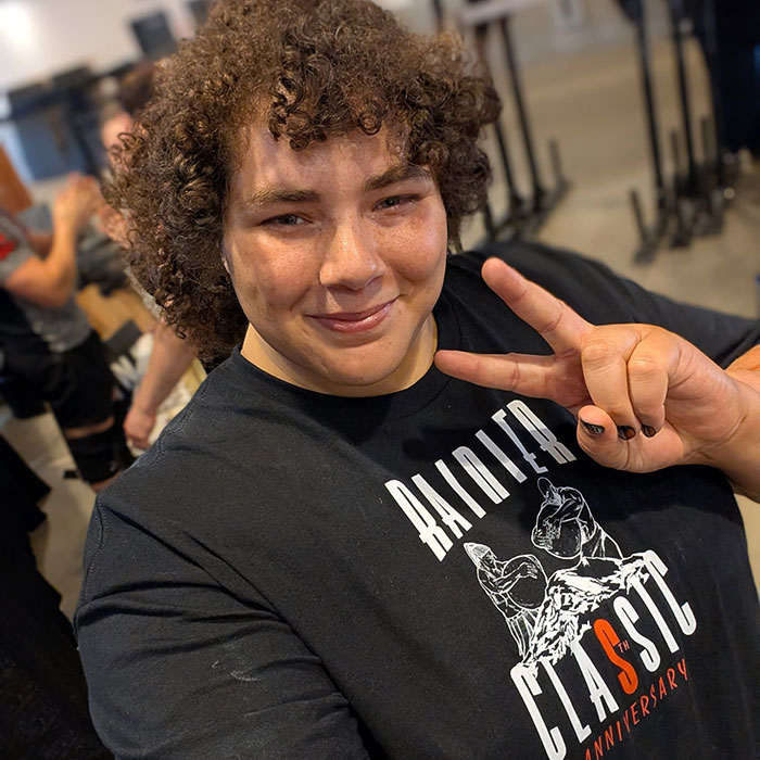 Person with curly hair wearing a black shirt and making a peace sign, linked to world’s strongest woman controversy. Person with curly hair wearing a black shirt and making a peace sign, linked to world’s strongest woman controversy.