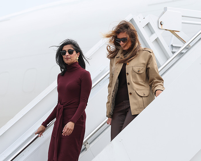 Two women wearing sunglasses descend an airplane staircase, with one in a maroon dress and the other in a tan jacket amid split rumors.