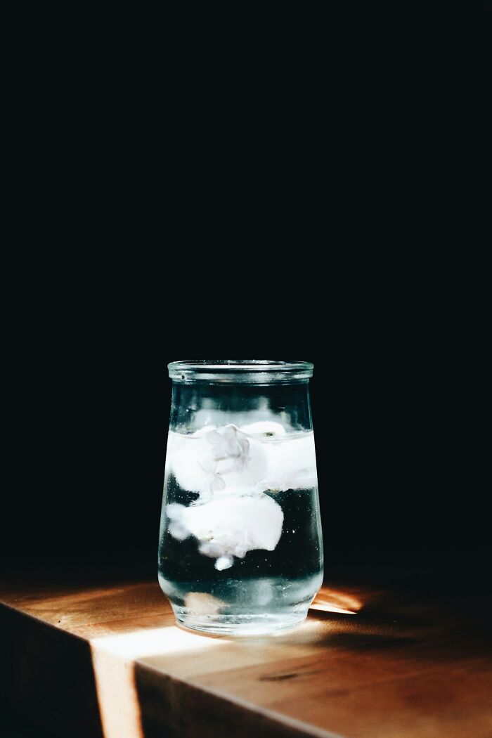 Glass of water with ice cubes on a wooden surface, bright contrast against dark background representing positive stereotypes.
