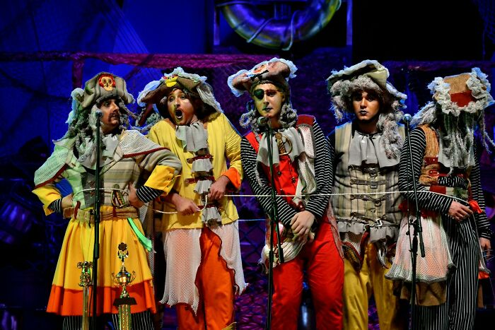 Performers in colorful theatrical costumes on stage, illustrating work secrets about baristas doctors and plumbers.