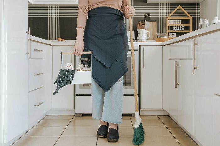 Person holding cleaning supplies and broom in modern kitchen illustrating surprising habits discovered about partner after moving in.