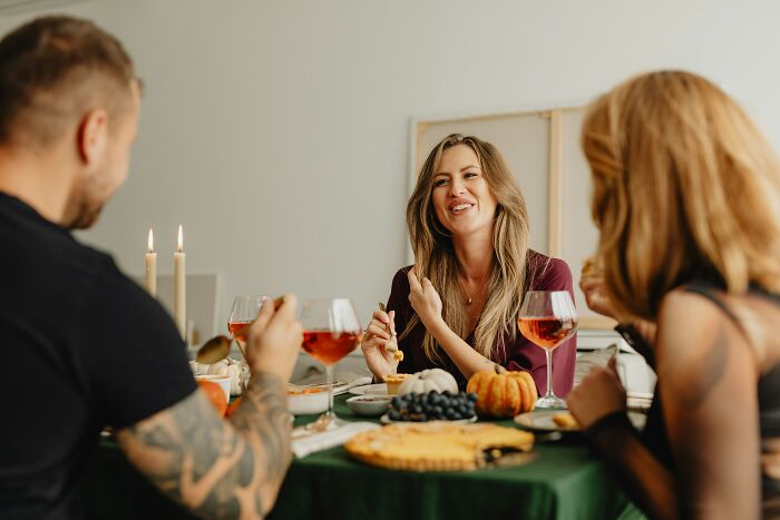 Three people sharing Thanksgiving dinner, enjoying food and drinks while discussing politics and mashed potatoes.