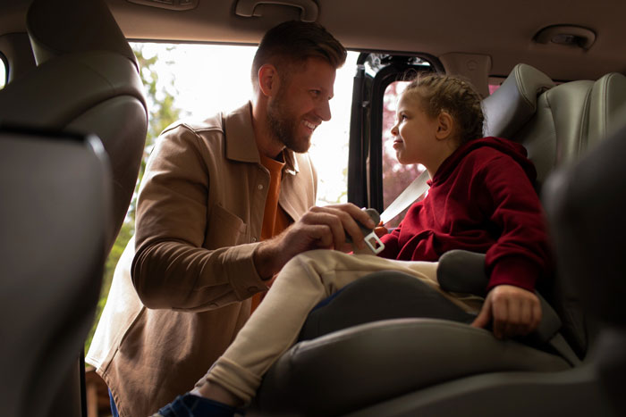 Man helping child in car seat, illustrating family tensions as mom prioritizes widowed friend over kids.
