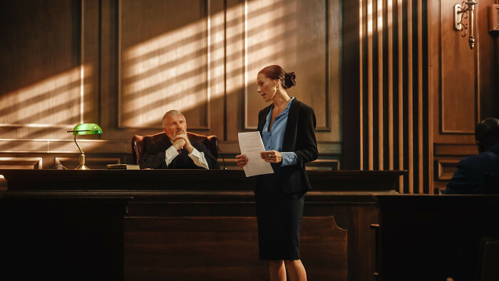 Female lawyer sharing interesting laws and loopholes in a courtroom with judge listening attentively behind bench.