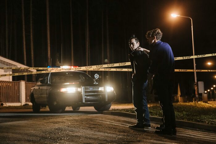 Police detain a suspect behind caution tape near a patrol car at night, illustrating lawyers sharing interesting laws and loopholes.
