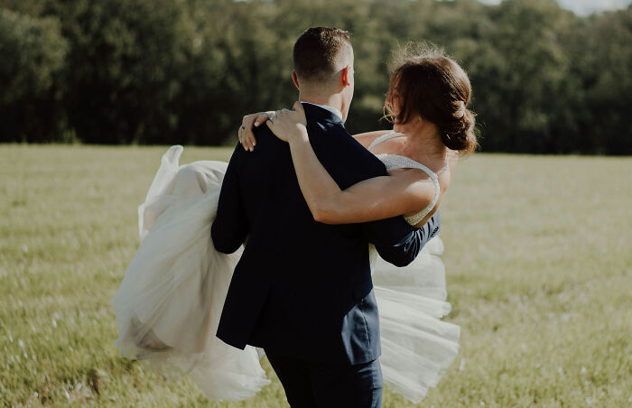 Groom carrying bride in a field, illustrating interesting laws and loopholes related to marriage and legal commitments.