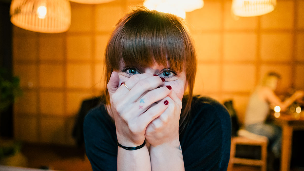 Young woman covering her face with hands in a cozy setting, reflecting on things learned embarrassingly late in life.