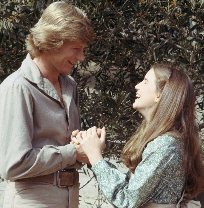 Melissa Gilbert and her on-screen husband holding hands outdoors, highlighting the age gap in their roles. Melissa Gilbert and her on-screen husband holding hands outdoors, highlighting the age gap in their roles.