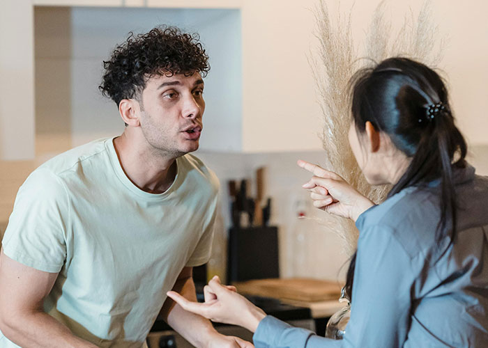 Man reacting strongly while discussing teen daughter’s relationship with woman in a home kitchen setting.